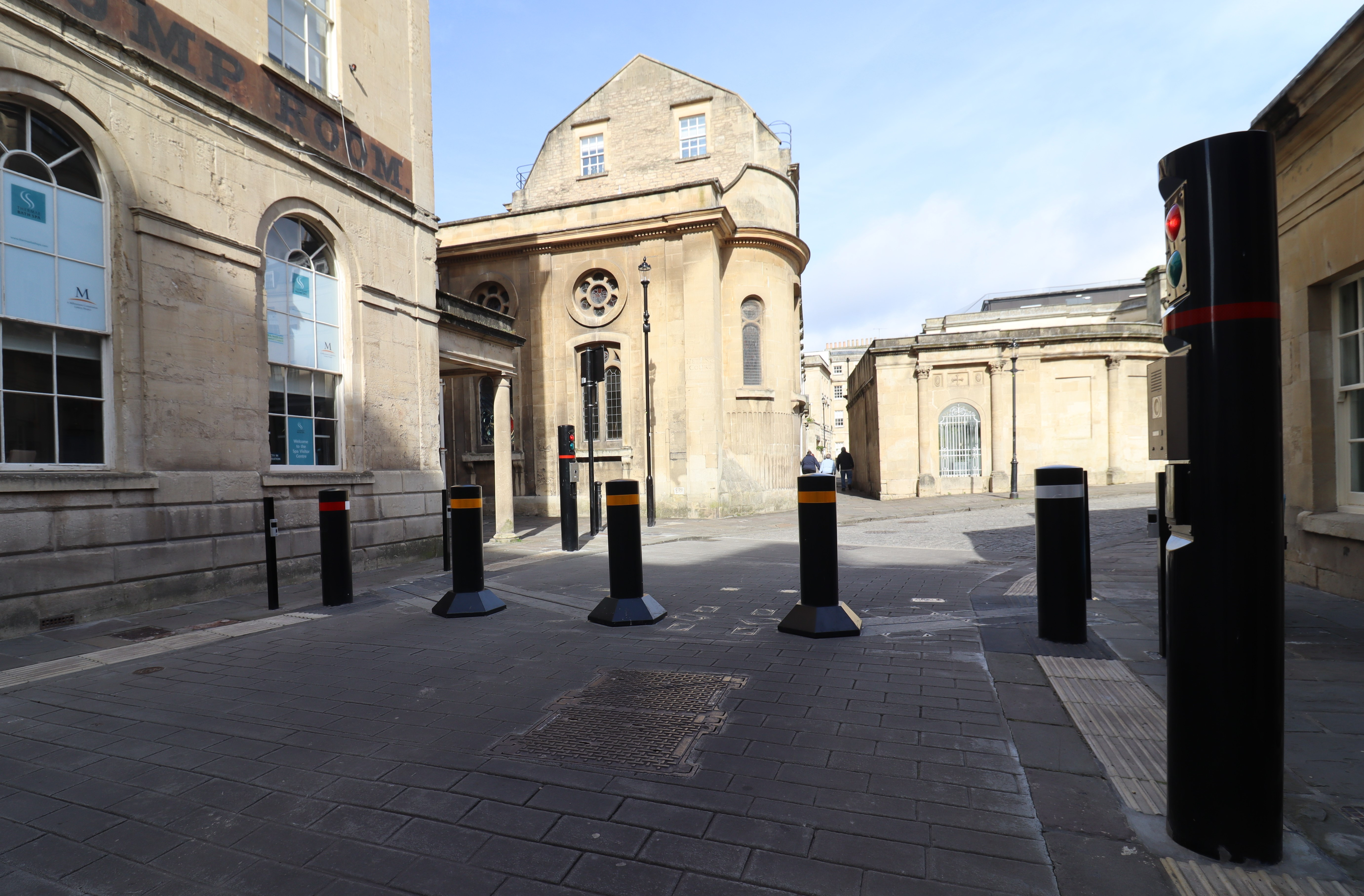 Black bollards with red and yellow bands on a paved street, surrounded by historic stone buildings and arched windows