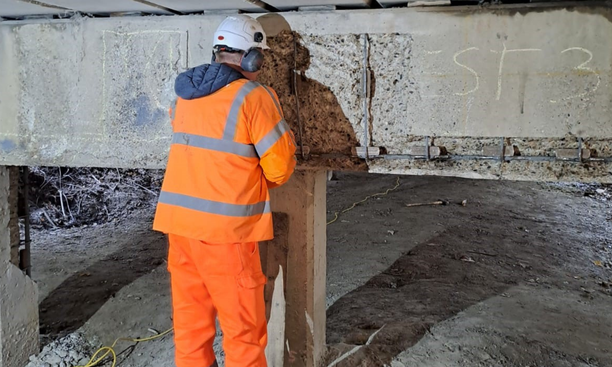 man in orange PPE with his back to the frame in front of a concrete beam