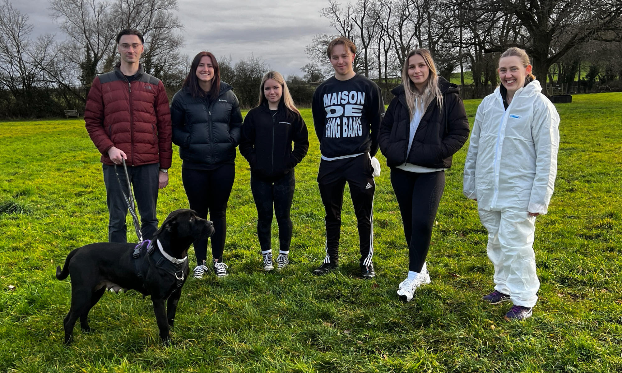 6 individuals facing front with a black dog on a lead to the left of the photo